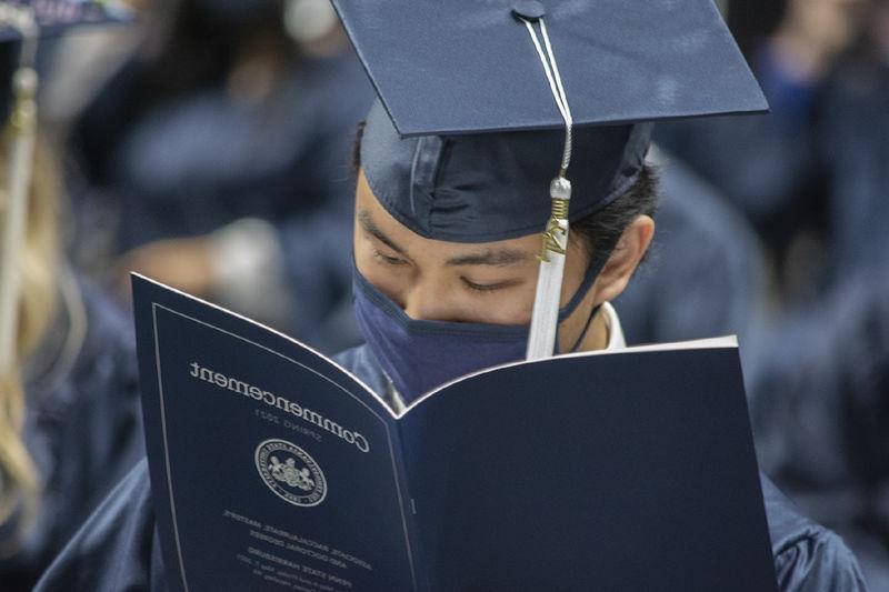 graduate in cap, gown, and face mask reading program