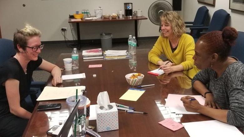 three women at a table smiling while reviewing papers